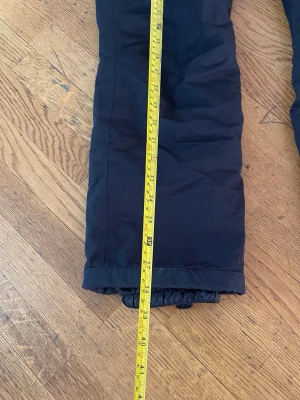 Svarta täckbyxor med resår - Svarta täckbyxor med rak passform och resår vid benslut. Perfekta för kalla dagar när du vill hålla dig varm och bekväm. Klassisk design som funkar till det mesta och är enkel att matcha med andra ytterkläder.