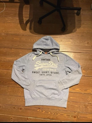 Superdry hoodie - En Hoodie från Superdry, Japan. Den ser grå ut på bilderna men den är ljusblå (se sista bilden). Storlek L men sitter bra på mig som brukar ha M