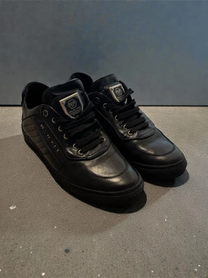 Philip plein skor - sneakers från Philipp Plein, tillverkade i Italien. Klassisk svart lo-top-modell i äkta läder med metall­detaljer och logotyp på sidan. Modellkod: 6642 2125 B. Köpta nya (original), och säljs nu på grund av att de inte används längre. Nypris 6 300kr
