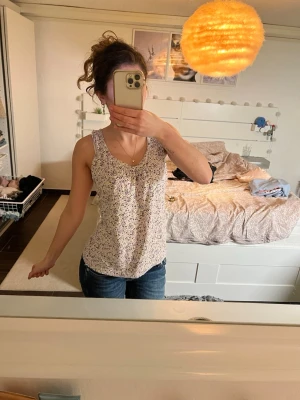 Blommig ärmlös linnetopp - Supersöt ärmlös linnetopp med småblommigt mönster i lila, grönt och vitt. Toppen har rundad halsringning. Linnet är från 365 Sunshine