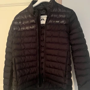 Svart J.Lindeberg jacka  - Snygg svart dunjacka från J.Lindeberg i storlek M. Jackan har ett stilrent, quiltat mönster och diskret logga på bröstet. Passar dig som är 175-180 cm lång🙂 Skriv om du har någon fundering!