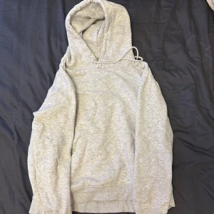 Ljusgrå hoodie från H&M i bomull - Säljer en enkel och stilren ljusgrå hoodie från H&M i mjuk bomull. Tröjan har huva med snörning och långa ärmar, perfekt för chill dagar. Klassisk passform och ribbade muddar vid ärmslut och nederkant.