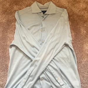 Ljusblå skjorta från Eton slim fit - Snygg ljusblå skjorta från Eton i slim fit-modell. Skjortan har klassisk krage, långa ärmar och knappar framtill. Materialet är mjukt och känns som bomull, perfekt för dig som gillar stilrena och fräscha plagg. Passar dig som vill ha en clean look.