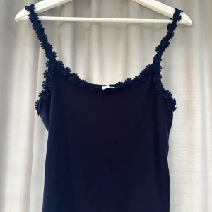 Mörkblå linnetopp med blommiga band - Supersöt mörkblå linnetopp från other stories med blommiga detaljer längs axelbanden och halsringningen. Toppen är ärmlös och har en enkel, rak passform. Stl M