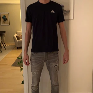 Blå Adidas t-shirt i bomull - Blå t-shirt från Adidas med klassisk rund hals och vit Adidas-logga på bröstet. Modellen är kortärmad och har en clean, enkel design som funkar till jeans eller shorts. Materialet är mjuk bomull som känns skönt mot huden.