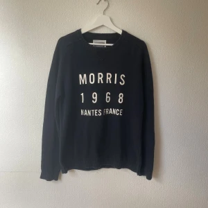 Svart tröja Morris Nantes France M - Svart långärmad tröja från Morris med tryck 'Morris 1968 Nantes France' på bröstet. Tröjan är tillverkad i 100% bomull och har ribbade muddar vid hals, ärmslut och nederkant. Perfekt för dig som gillar klassisk och stilren design.