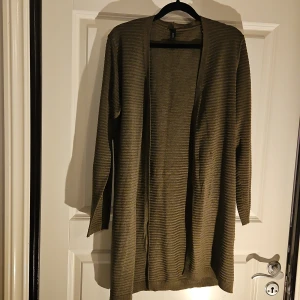 Randig mörkgrön kofta från Soyaconcept - Säljer en mörkgrön kofta från Soyaconcept. Koftan har en öppen front utan knappar och är tillverkad i ett stickat material med diskreta horisontella ränder. Långärmad och loose passform.