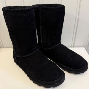 Svarta Bearpaw boots i mocka - Svarta boots från Bearpaw i mjuk mocka med hög skaft och grov sula. Skorna har rund tå och är fodrade för extra värme, perfekta för kyliga dagar. Klassisk design med diskret logga bak på hälen. Har använts några gånger, men i fint skick.