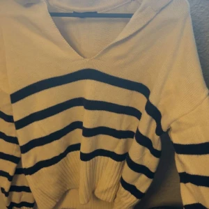 Randig beige hoodie med huva - Snygg beige hoodie med mörkblå ränder och huva. Tröjan är stickad och har en avslappnad passform med ribbad nederkant. Perfekt för dig som gillar en chill och stilren look. V-ringad hals och långa ärmar ger extra komfort.