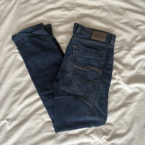 Blå jeans Gardeur Nevio-6 regular fit - Snygga blå jeans från Gardeur, modell Nevio-6 med regular fit. Klassisk femficksdesign, raka ben och diskreta kontrastsömmar på bakfickan. Jeansen är tillverkade i slitstarkt denim och har dragkedja och knapp framtill. Perfekt passform för dig som gillar stilrena jeans.