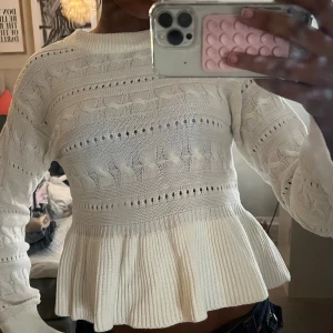 Vit stickad tröja med volang - Supersöt vit stickad tröja med volang nedtill och snygga hålstickade detaljer. Tröjan har långärmade ärmar och en croppad passform som ger en trendig look. Perfekt att styla med jeans eller kjol för en chill vibe.