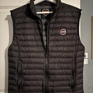 Svart dunväst från Colmar - Snygg svart dunväst från Colmar med quiltad design och dragkedja framtill. Västen har två praktiska fickor med dragkedja och en hög krage. Perfekt för lager-på-lager och stilren look.Använd ett fåtal gånger men har legat i en garderob ett tag.