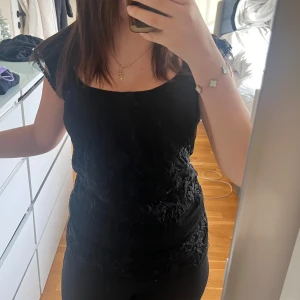 Svart blommig blus med spetsdetaljer - Säljer en svart blus med blommigt broderade spetsdetaljer. Toppen har en rundad halsringning och är ärmlös med fina spetskanter vid axlarna. Materialet är lätt och ger en elegant känsla. Perfekt för dig som gillar detaljer och svart.