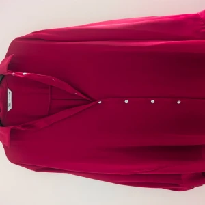 Röd satin oversized skjorta från Zara - Snygg röd satin skjorta från Zara i oversized modell med klassisk krage och vita knappar framtill. Skjortan är tillverkad i ett mjukt och lätt polyestertyg som ger ett skönt fall. Perfekt för dig som gillar en loose och chill stil. 