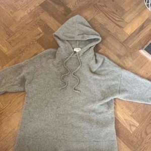 Grå kashmir hoodie från Soft Goat - Säljer en supermjuk och lyxig grå hoodie från Soft Goat, tillverkad i 100% kashmir. Den har en bekväm passform med ribbade muddar och en justerbar huva med snören. Passar även M