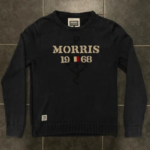 Svart tröja från Morris - Snygg svart tröja från Morris med texten 'Morris 1968' på framsidan. Tillverkad i 100% bomull, perfekt för en stilren look. Tröjan har långa ärmar och ribbade muddar vid ärmslut och nederkant.