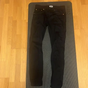 Svarta jeansbyxor från 157, storlek M - Svarta jeansbyxor från 157 i storlek M. Modellen har klassisk femficksdesign med silverfärgade nitar och knapp, samt smal passform som sitter snyggt längs benen. Materialet är mjukt och följsamt jeans, perfekt för en clean och stilren look.