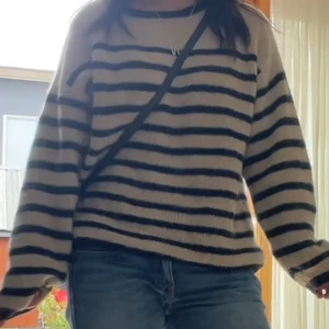 Randig stickad tröja från Soaked in Luxury  - Säljer en beige och svart randig stickad tröja från Soaked in Luxury. Tröjan har en loose passform, rund halsringning och långa ärmar. Perfekt för dig som gillar en chill och stilren look.