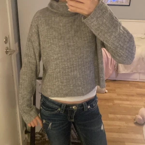 Grå ribbad polotröja i stickat material - Mysig grå polotröja med ribbat mönster och lång ärm. Tröjan är stickad och har en hög polokrage som ger en chill vibe. Perfekt till jeans eller kjol för en enkel men snygg look. Inte använt så många gånger, den är i väldigt bra skick💕