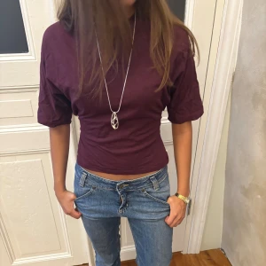 Mörkröd topp - Säljer en mörkröd croppad topp med halvärm och hög hals. Toppen har en slim passform och är tillverkad i mjuk bomull. Perfekt att styla med jeans eller kjol för en trendig look.