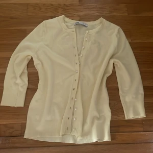Ljusgul kofta från zara  med pärlknappar - Säljer en ljusgul kofta från zara med fina pärlknappar framtill. Koftan har trekvartsärm och är tillverkad i mjuk bomullsblandning. Perfekt att slänga över en topp för en fräsch och stilren look.