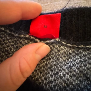 Stickad tröja HUGO med logomönster - Säljer en stickad tröja från HUGO i storlek M. Tröjan är beige med svarta detaljer och har ett coolt all-over logomönster. Rund hals och svarta muddar vid ärmslut och nederkant. Perfekt för dig som gillar streetstyle och vill sticka ut.