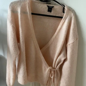 Ljusrosa omlottkofta från Lindex XS - Supermysig ljusrosa kofta från Lindex i storlek XS. Koftan är stickad och har omlottmodell med knytband i midjan och v-ringad hals. Långa ärmar och mjukt fluffigt material.