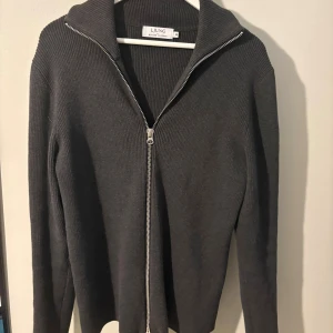 Mörkgrå stickad kofta från Ljung - Snygg mörkgrå stickad kofta från Ljung med ribbad struktur och hel dragkedja framtill. Koftan har en hög krage och långa ärmar, perfekt för lager på lager. Enkel och stilren design som funkar till många olika looks. Mitt pris: 699 butikspris/nypris:1799kr. Bredd:48cm Längd:65cm. Priset är hugget i sten, skriv vid funderingar 