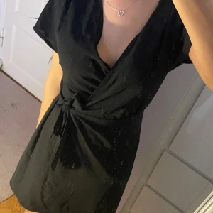 Svart omlott klänning - Elegant svart klänning i omlottmodell med korta ärmar och knyt i midjan. Ger en smickrande form och är perfekt både till vardag och fest ✨ Fint skick. 💬 Pris kan diskuteras!  🖤 En tidlös klänning som alltid funkar – enkel, feminin och stilren!