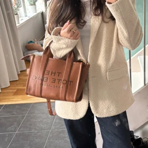 Brun Marc Jacobs väska - Säljer denna superfina tote bagen från Marc Jacobs i ett bra skick. Inga defekter eller liknande på väskan. Köptes för ca 4000 kr