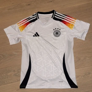Tysklands fotbollströja Adidas herr - Säljer en officiell Tyskland fotbollströja från Adidas. Tröjan är vit med svarta detaljer, Tysklands flagg färger på axlarna samt broderat landslagsmärke och fyra stjärnor på bröstet. Riktigt fräsch inte använt nån gång typ. Pris går såklart o diskuteras även så om man har några frågor:)