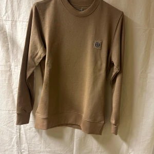 Brun sweatshirt från River Island - Snygg beige / brun sweatshirt från River Island med rund hals och lång ärm. Tröjan har ett stilrent märke på bröstet och är tillverkad i mjuk bomull. Perfekt för dig som gillar enkel och clean stil. Passar dig som vill ha en normal passform. Storlek: S,M,L,XL,XXL. Skriv önskad storlek efter lagd order. 