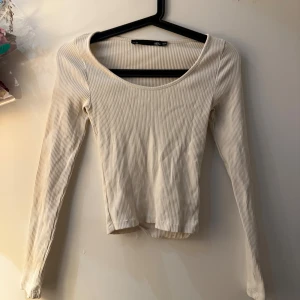 Ribbad beige långärmad topp 157 - Säljer en beige ribbad långärmad topp från 157 med rundad halsringning. Toppen har en slim passform och är tillverkad i mjuk bomull. Perfekt för dig som gillar enkla och stilrena plagg med lite struktur. Passar dig som vill ha en basic topp med snygg ribbad yta.