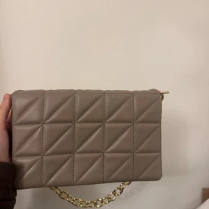 Beige quiltad axelväska med kedja - Snygg beige axelväska med guldig kedja. Köpt från shein för ett tag sen, använts ett fåtal gånger och är fortfarande i väldigt bra kvalité. 