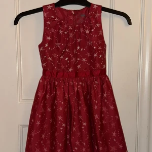 Röd stjärnmönstrad klänning från Name It - Supersöt röd ärmlös klänning från Name It med vita stjärnor över hela tyget. Klänningen har rund halsringning, markerad midja och lätt utställd kjol. Skickar ditt köp inom 24h💘