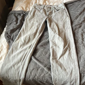 Ljusgrå raka jeansbyxor - Säljer ett par ljusgrå jeansbyxor med klassisk femficksdesign och raka ben. Byxorna har normal passform och är tillverkade i bomullstyg. Snyggt slitna detaljer vid benslut och och lite gula fläckar. Vi tvättar innan vi säljer. Jag säljer dem för att dem är förstora för mig. Knappt använda 