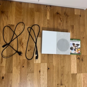 Xbox One S - Xbox One S i fint skick, komplett med strömkabel, HDMI-kabel och spelet Overwatch. Konsolen är vit och visar endast minimalt slitage. Perfekt för gaming och underhållning. Allt fungerar som det ska.