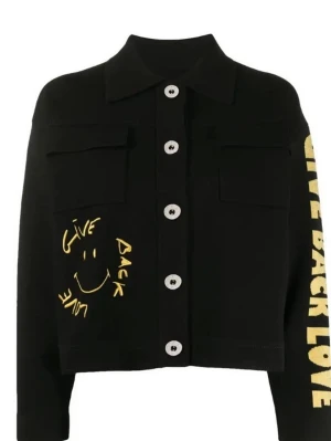 Svart Jacka med tryck från Sandro  - Cool svart oversize jacka med stora knappar och tryck i gult och vitt. Framsidan har bröstfickor och ett handskrivet smiley-motiv med texten 'Give Back Love'. På ena ärmen står samma text i gult och på ryggen finns en stor rund patch med smiley och text.