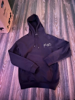 Stilren hoodie strl XS men passar folk med M - Svart hoodie från Your Turn med vit logga tryckt både fram och stort på ryggen. Tröjan har huva med snörning och långa ärmar. Mjuk och skön bomullsmix som passar perfekt när du vill ha en chill och stilren look.