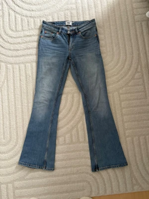 Blå bootcut jeans från 157 XS - Bootcut jeans från 157 i ljusblå tvätt med klassisk femficksdesign och låg midja. Modellen är bootcut med utsvängda ben och har orangea sömmar. Materialet är jeans och passformen är normal. Perfekt för dig som gillar retrovibbar och vill ha ett par snygga blå jeans. Dom är i short 