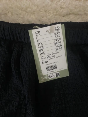 Mörkblå volangkjol med resår - Säljer en mörkblå kortkjol med volang och resår i midjan. Kjolen har en snygg struktur i tyget och är perfekt för dig som gillar enkel men cool stil. Passar dig som är 8-10 år men såklart äldre också och vill ha något bekvämt och trendigt.