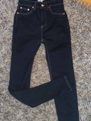 Mörkblå skinny jeans med hög midja - Säljer ett par mörkblå skinny jeans med hög midja och klassiska kontrastsömmar. Jeansen har fem fickor, bälteshällor och knappgylf. Perfekta för dig som gillar en tight passform och stilren look.