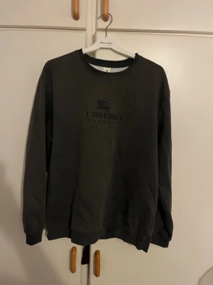Svart sweatshirt från Burberry - Säljer en svart sweatshirt från Burberry med klassisk logga och texten 'Burberry London' på bröstet. Tröjan har rund halsringning och långa ärmar. Perfekt för dig som gillar stilrena och exklusiva plagg.
