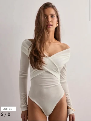Vit omlott bodysuit med offshoulder - Säljer en stilren vit bodysuit med omlott-detalj och offshoulder-design. Långärmad och figurnära passform som ger en snygg siluett. Perfekt att styla med jeans eller kjol för en trendig look. Kvar prislapp.