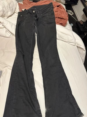 Svarta bootcut jeans från weekday - Svarta jeans från weekday med bootcut-snitt och klassisk femficksdesign. Jeansen har en mörk tvätt, dragkedja och knapp framtill samt BonBon-logga i rosa på bakfickan. Materialet är jeans med en mjuk känsla och passformen är normal.