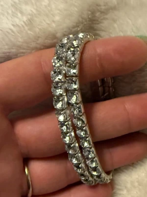 Armband - Bilden visar ett smycke, troligen ett armband med glittriga stenar, 