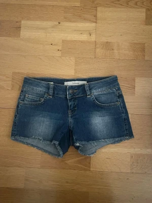 Blå jeansshorts från Subdued - Säljer ett par blå jeansshorts från Subdued med fransig kant. Shortsen har normal passform snygga detaljer på bakfickorna. Perfekta för varma dagar och chill stil.