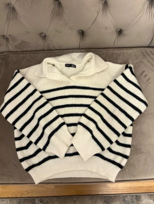 Vit och svart randig stickad tröja Dazy - Säljer en stickad tröja från Dazy i storlek M. Tröjan är vit med svarta horisontella ränder, har en bred krage och långa ärmar. Ribbstickad struktur ger en mysig känsla och passformen är normal. Perfekt för kyliga dagar!