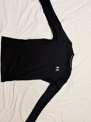 UNDER ARMOUR COMPRESSION - Bilderna visar en svart långärmad tröja från Under Armour, tillverkad i syntetmaterial och designad för träning. Tröjan har en rund hals och logotypen syns både fram och bak. Passar perfekt för sportaktiviteter