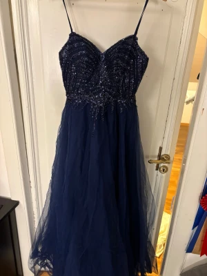Marinblå glittrig balklänning  - Säljer en marinblå balklänning med smala axelband och glittrig. Perfekt för bal eller speciella tillfällen. Snygg och elegant look som verkligen sticker ut. Den är endast använd en gång 